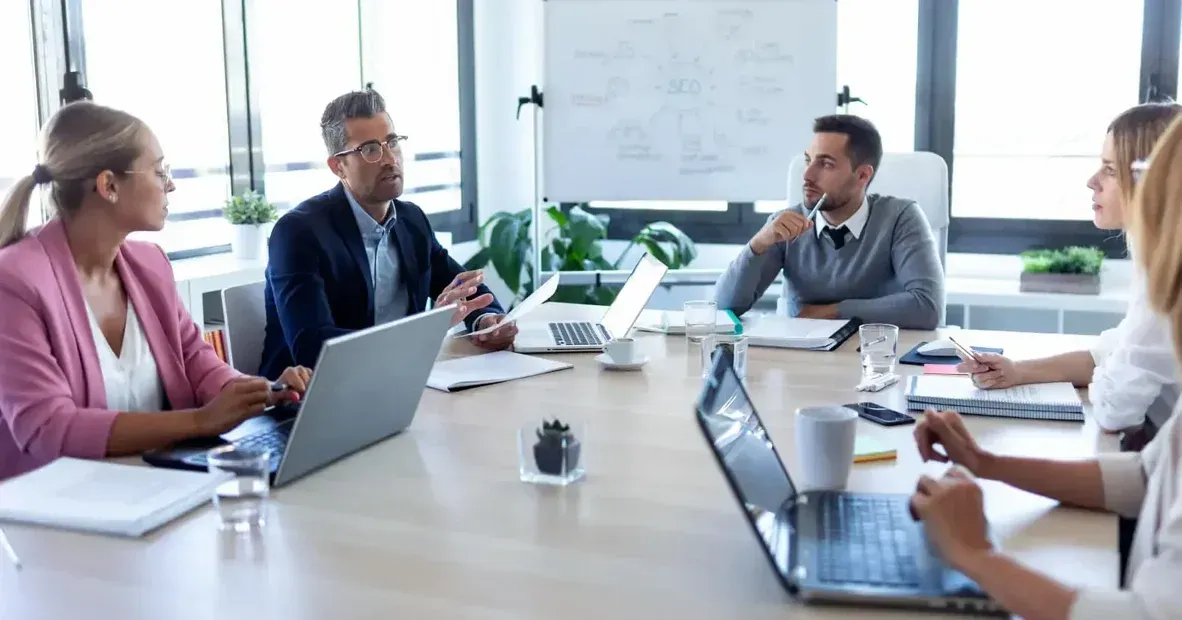A group of people are sitting around a conference table with laptops. A group of people are sitting around a conference table with laptops.