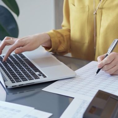Person typing on a laptop and writing notes on paper at a desk.