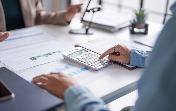 Hands using a calculator on a desk with charts and a laptop in a bright office