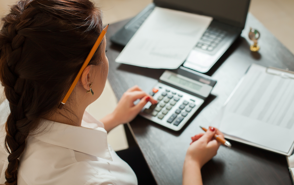 Person working at a desk with a calculator, laptop, and paperwork