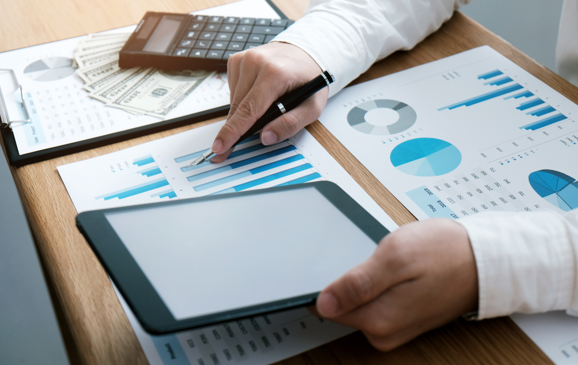 Hands analyzing business charts on a desk with a tablet and calculator