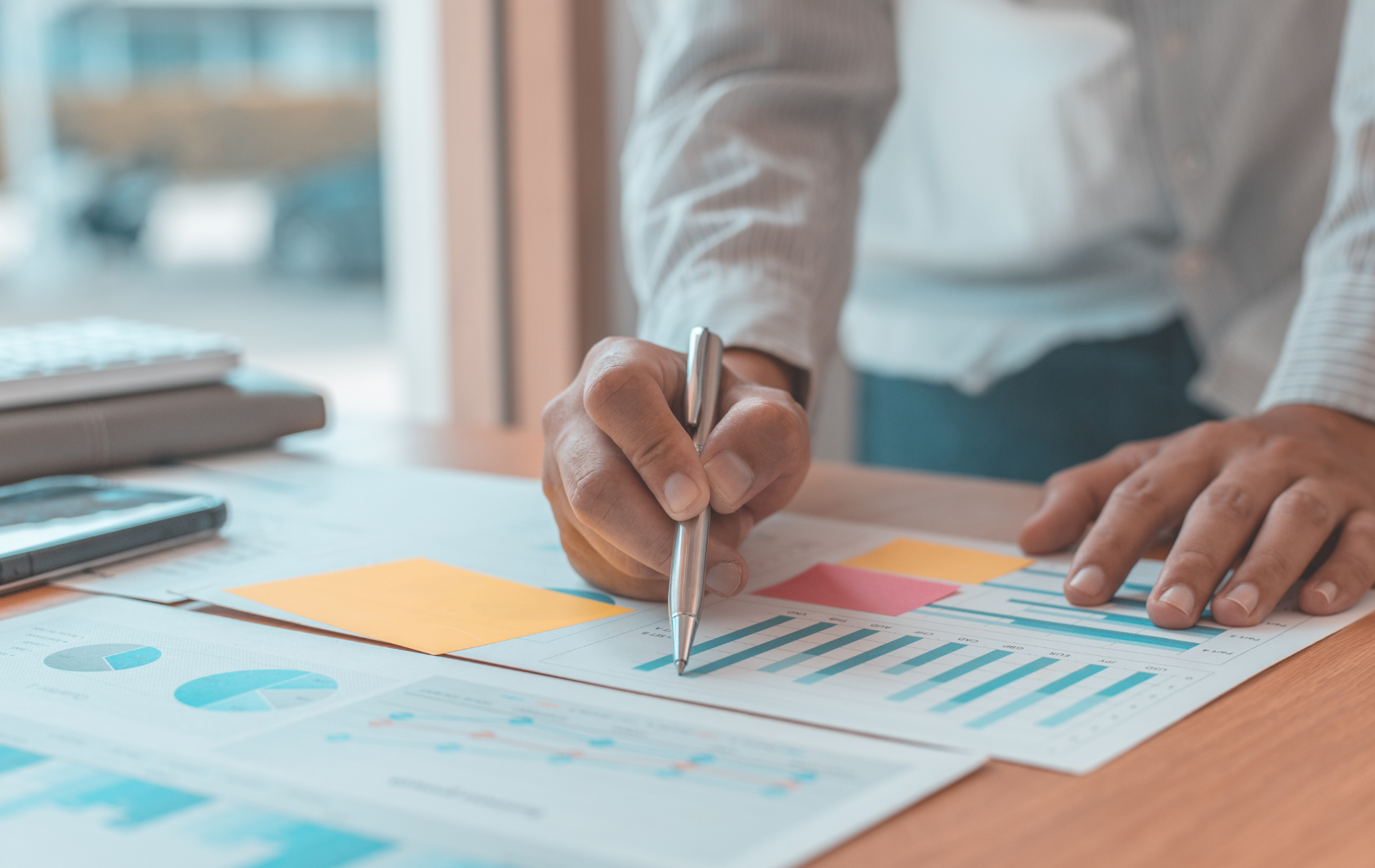 Hands marking charts on a desk with colorful graphs and a laptop nearby