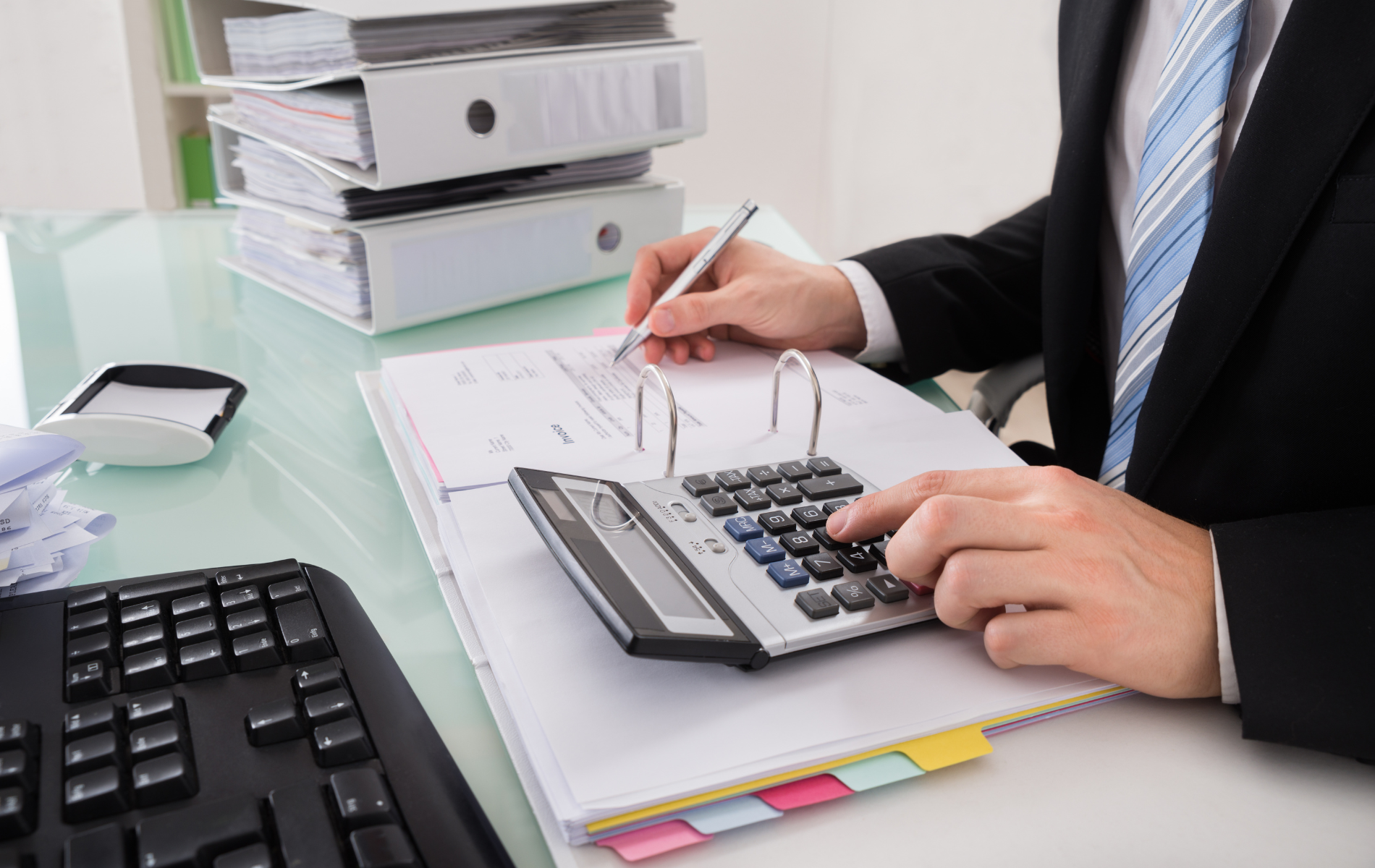 Person calculating on a desktop calculator beside paperwork in an office desk setup