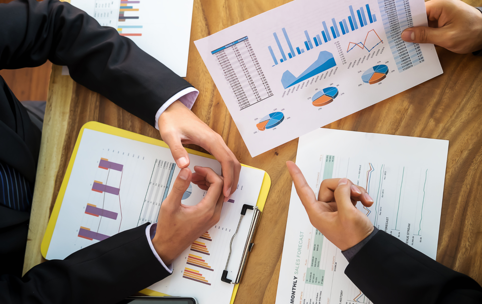 Business meeting with hands reviewing charts and graphs on a wooden table