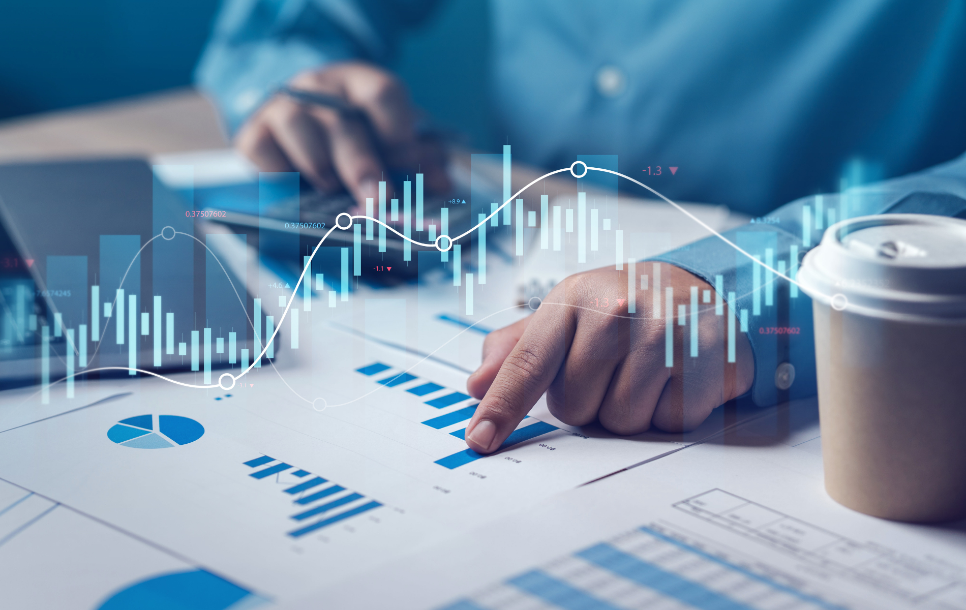 Person analyzing financial charts with a coffee cup nearby and digital graph overlays on a desk