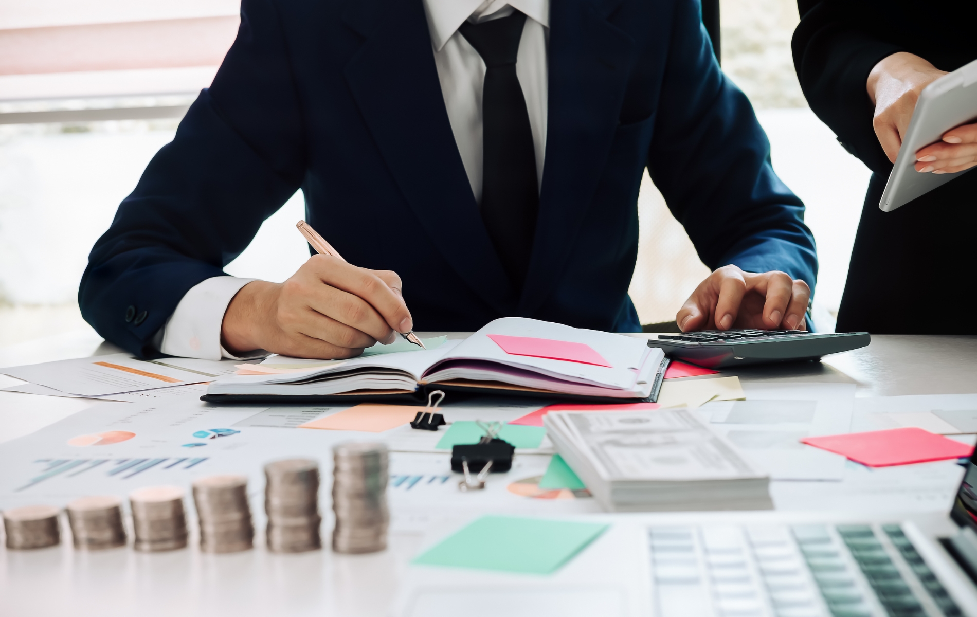 Business people reviewing financial documents at a desk with charts, calculator, and stacks of coins