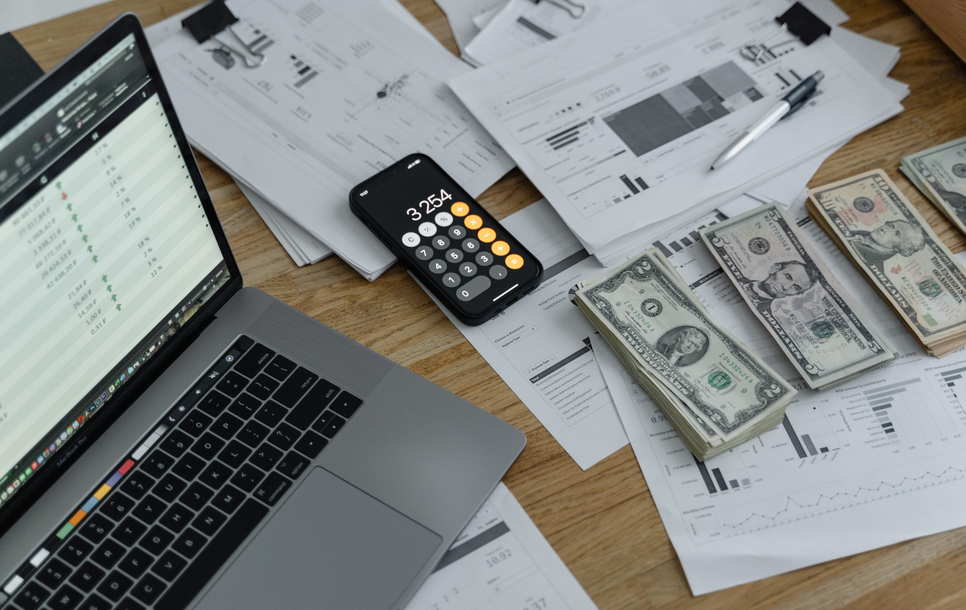 Laptop, calculator, bills, and financial paperwork on a desk with scattered money.