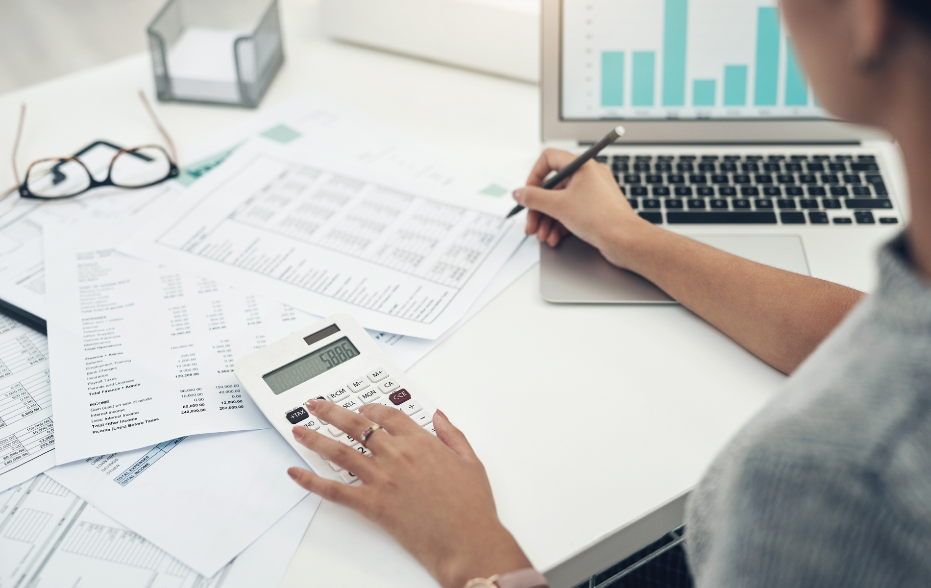 Person reviewing charts and spreadsheets at a laptop on a white desk