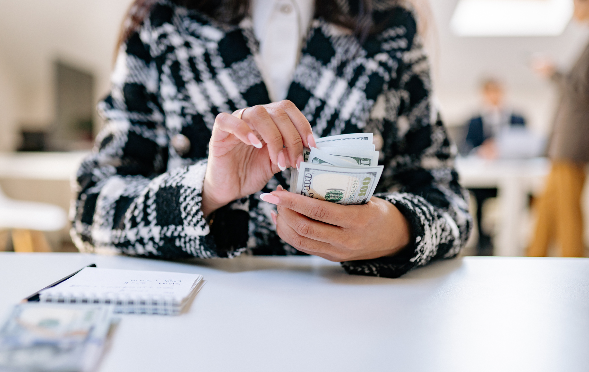 Person counting cash at a table, with a notebook beside them in a bright indoor setting