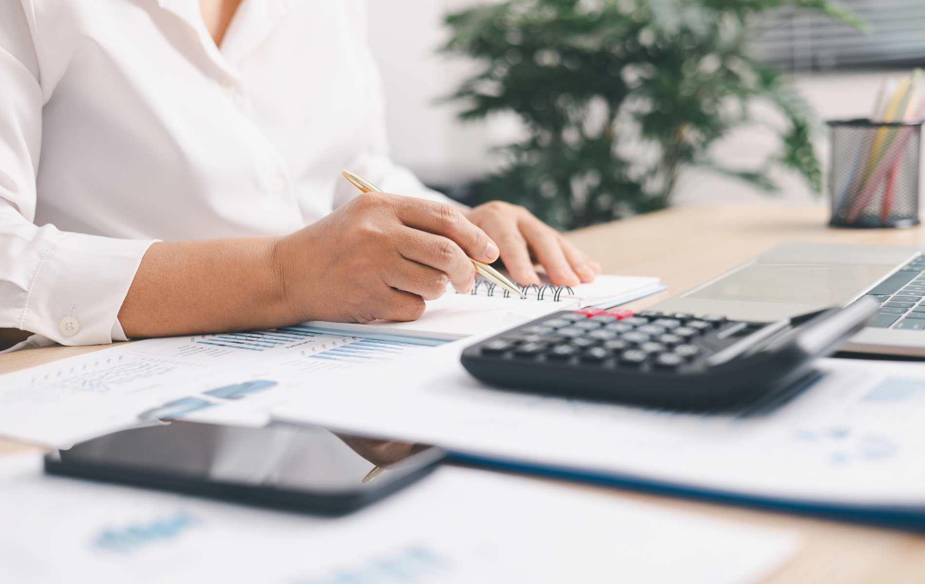 Person writing on paper at a desk with a calculator and smartphone nearby