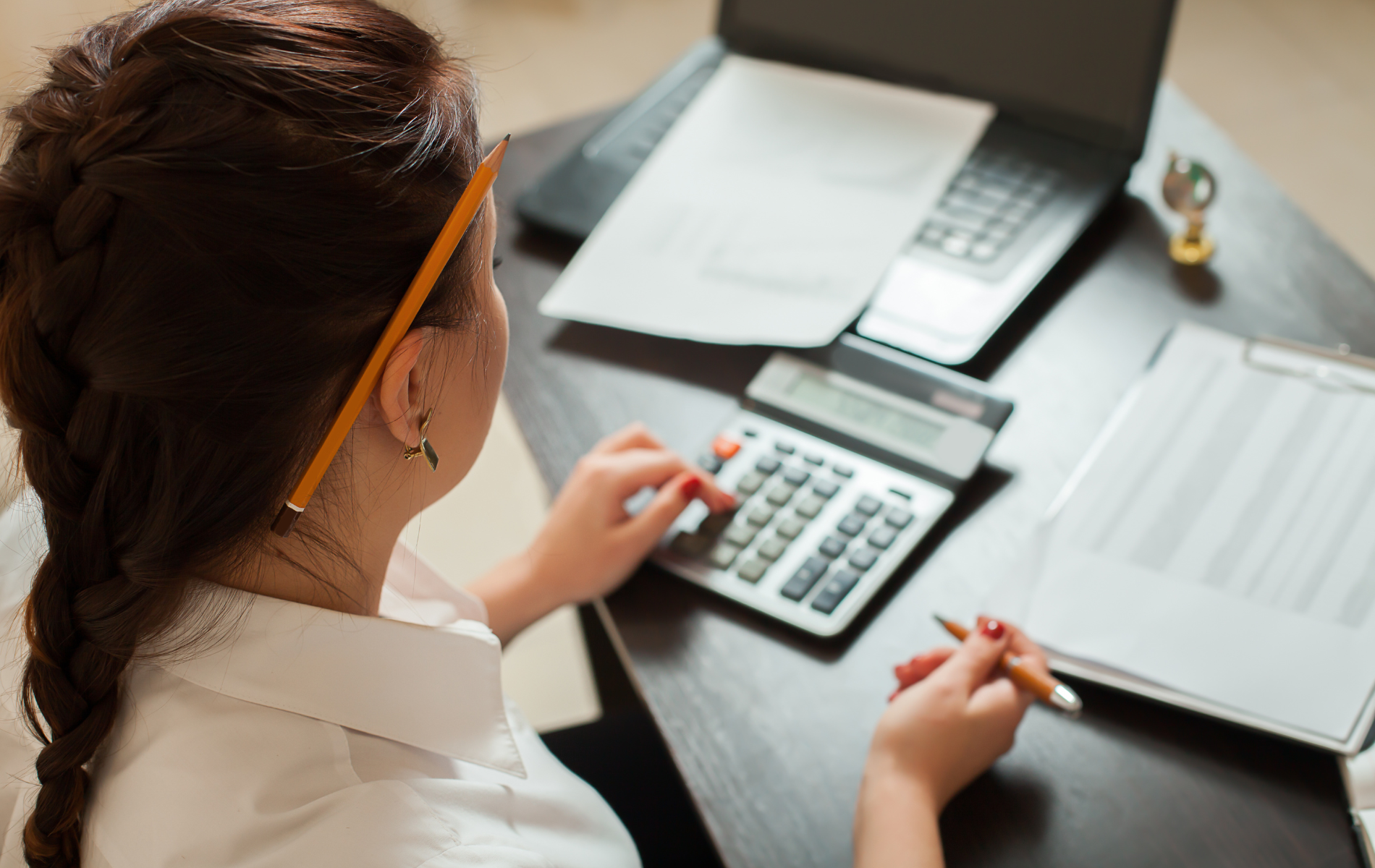 Person using a calculator at a desk with a laptop and papers.