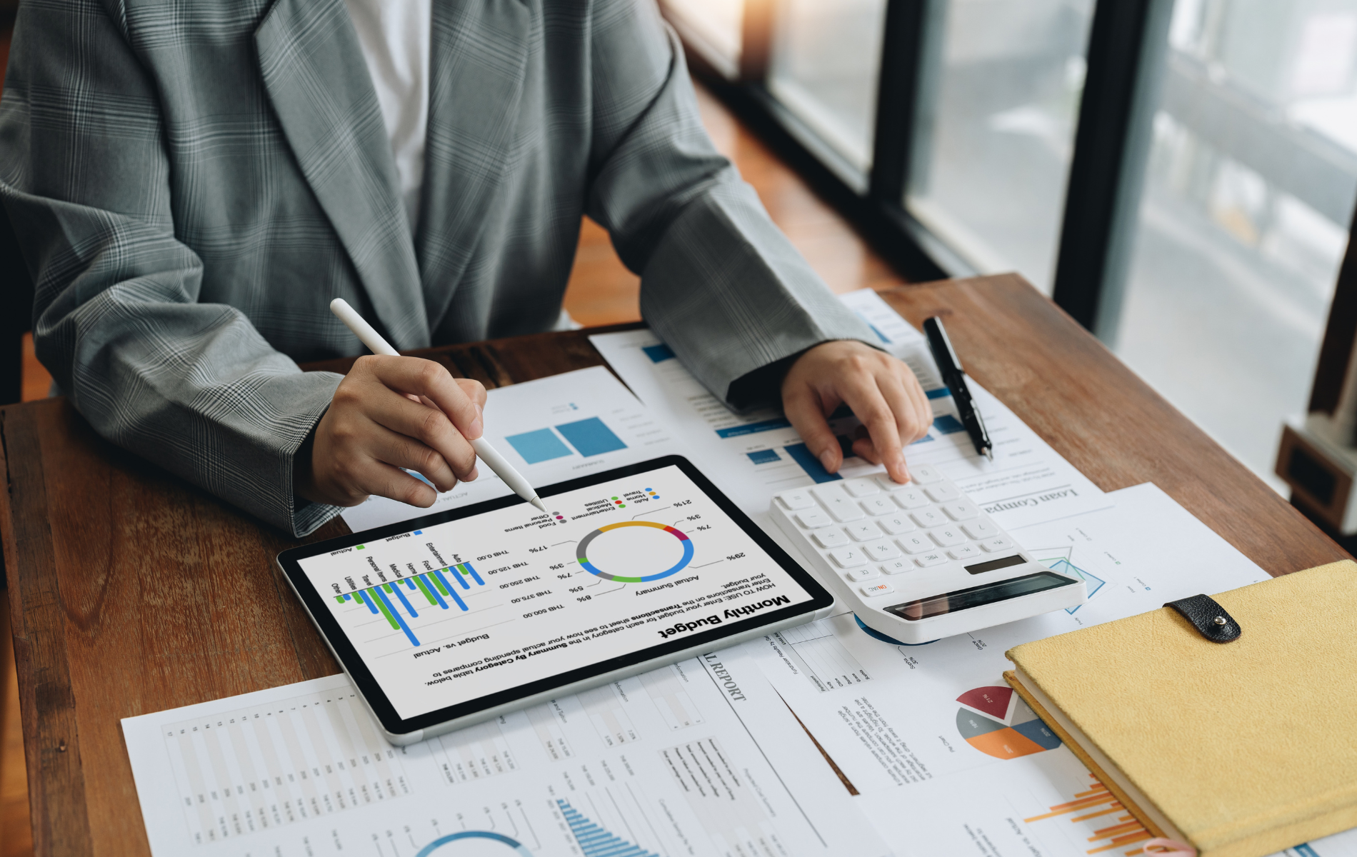 Person analyzing business charts on a tablet and paperwork at a desk with a calculator and pen