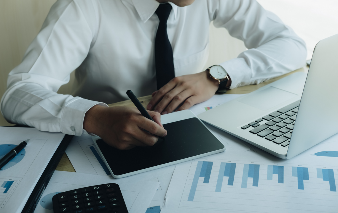Business person reviewing charts and notes at a desk with a laptop and calculator