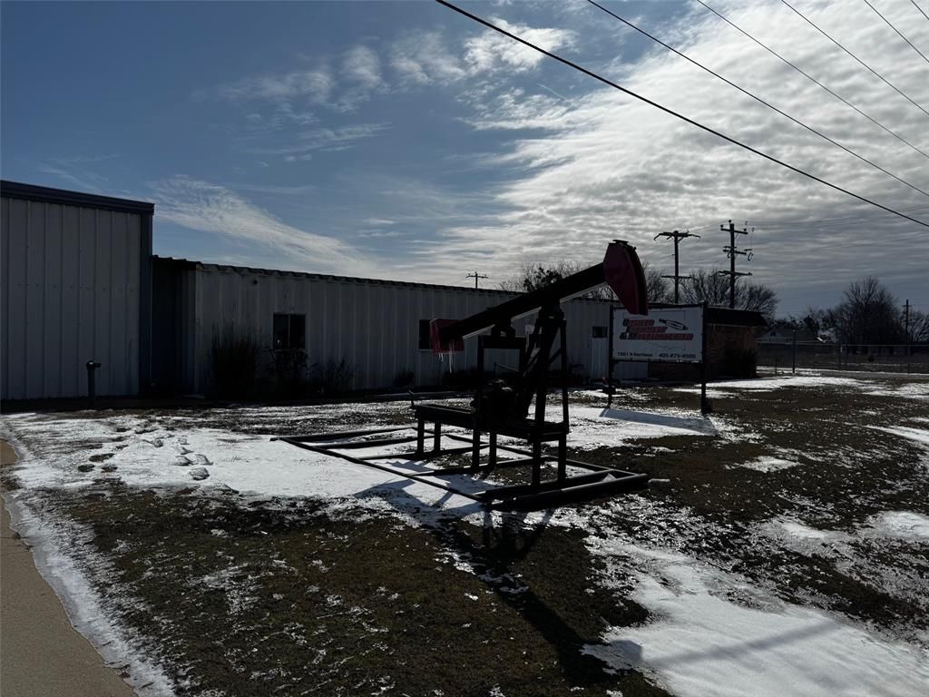 An oil pump is in the middle of a snowy field in front of a building.