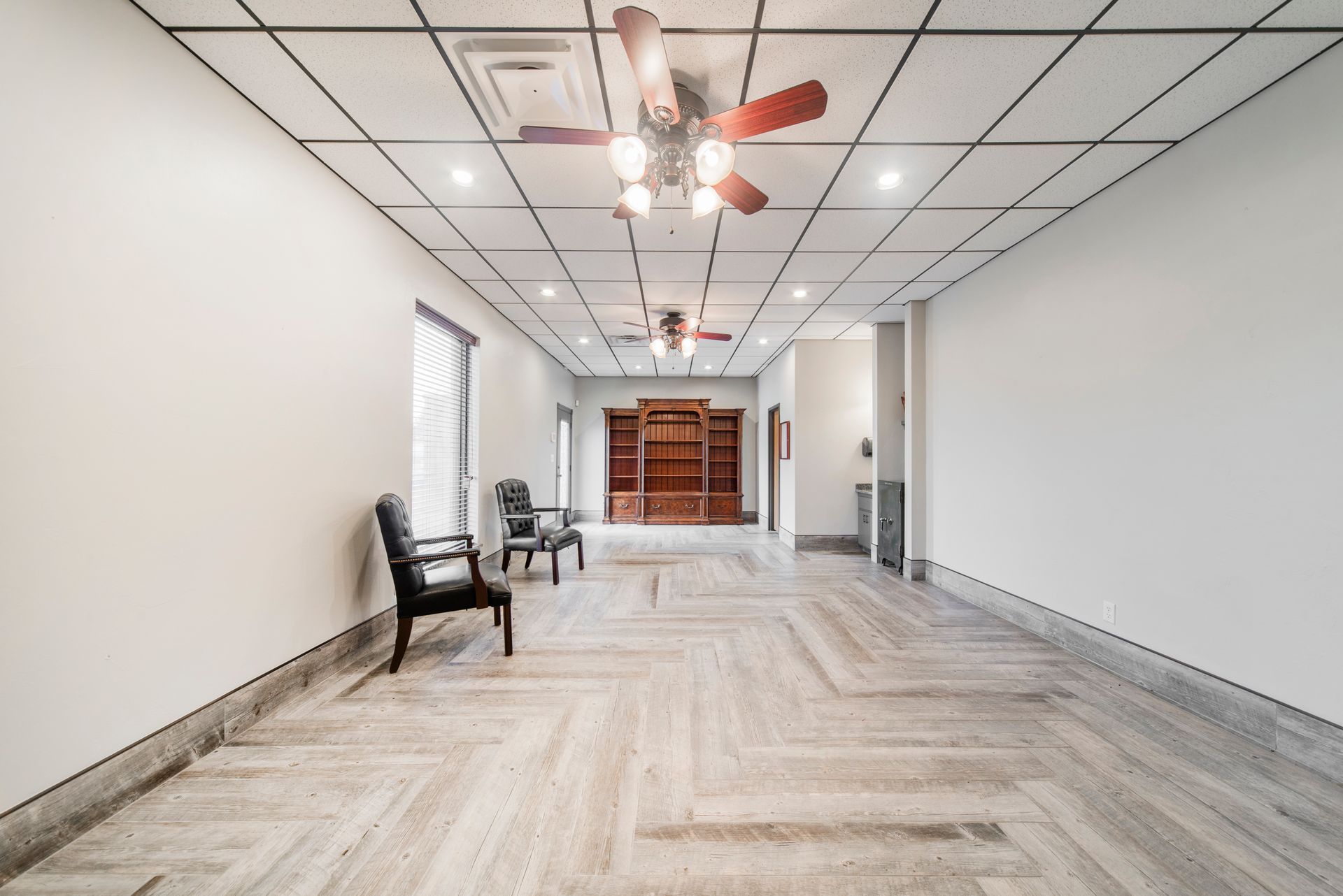 A large empty room with a ceiling fan and chairs