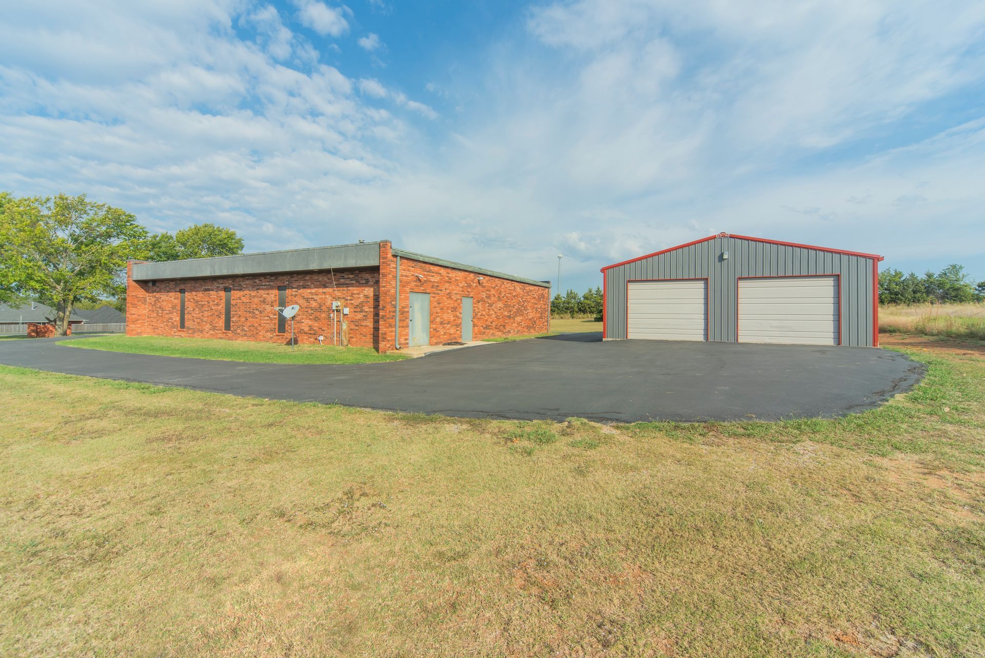 A brick building and a metal building are next to each other in a field.