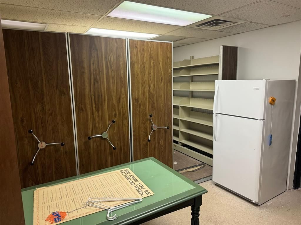 A room with a table , shelves , and a refrigerator.