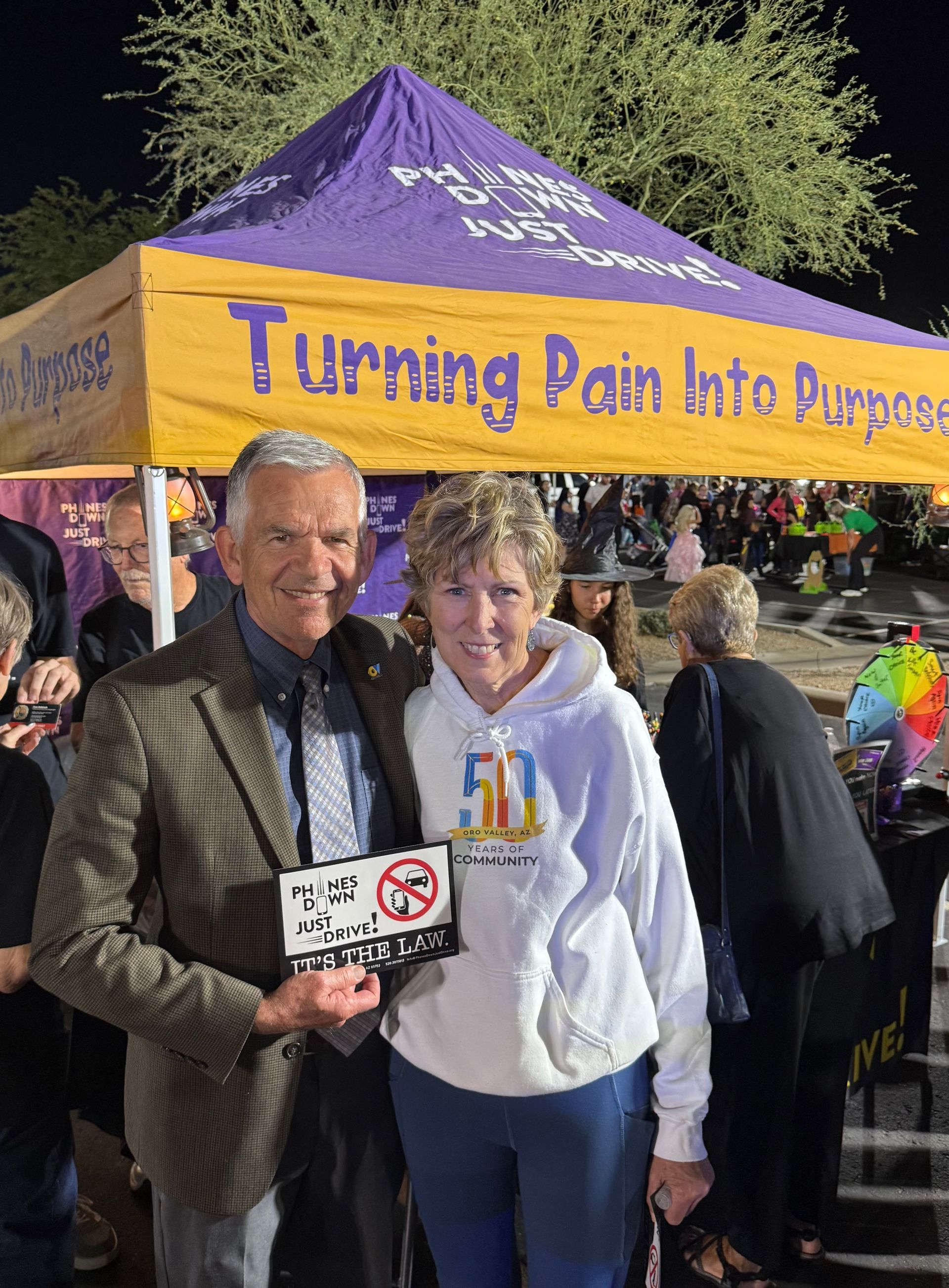 Man and woman stand smiling under a tent that reads