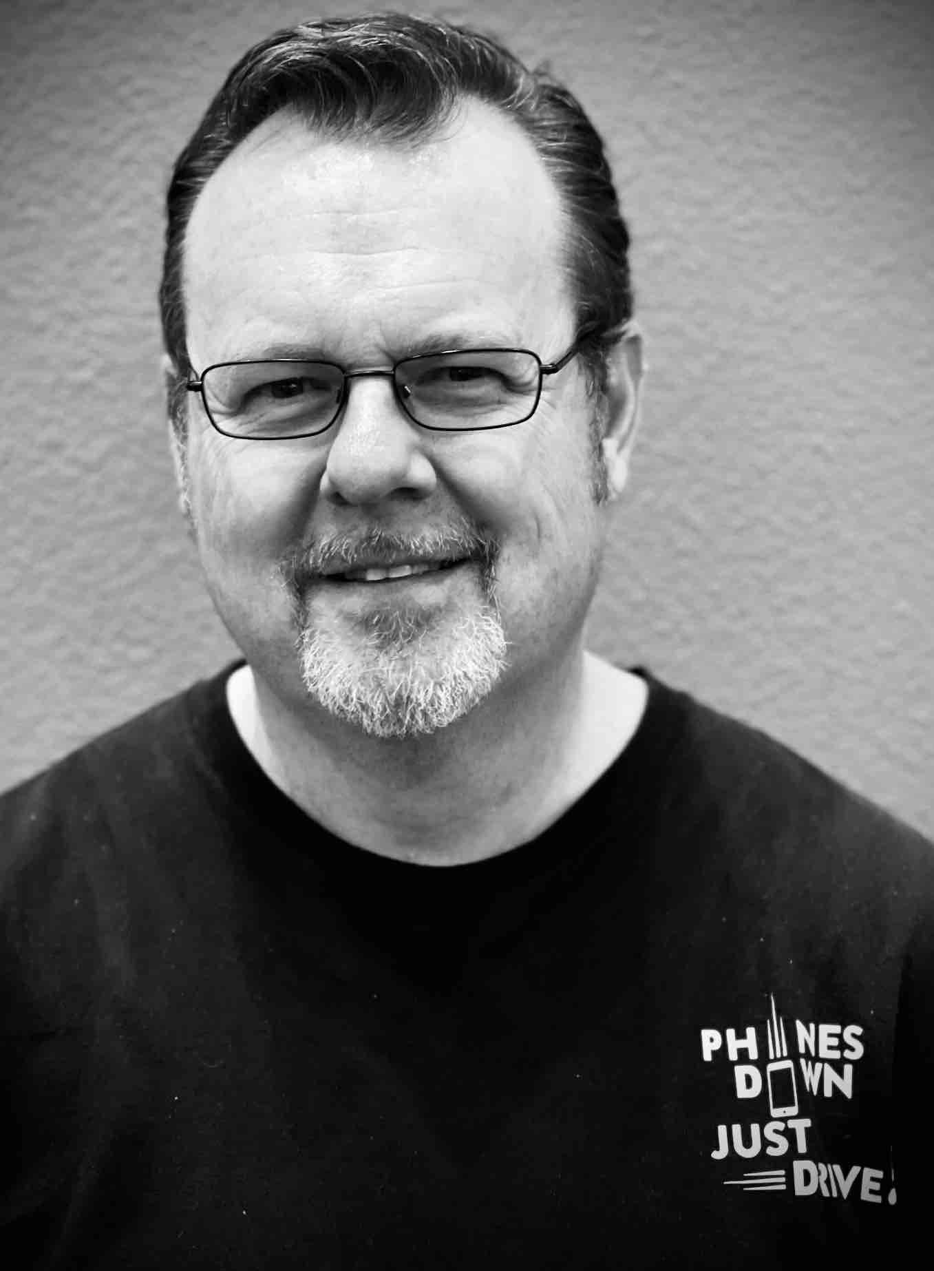 A man wearing glasses and a black shirt that says phones down just dive
