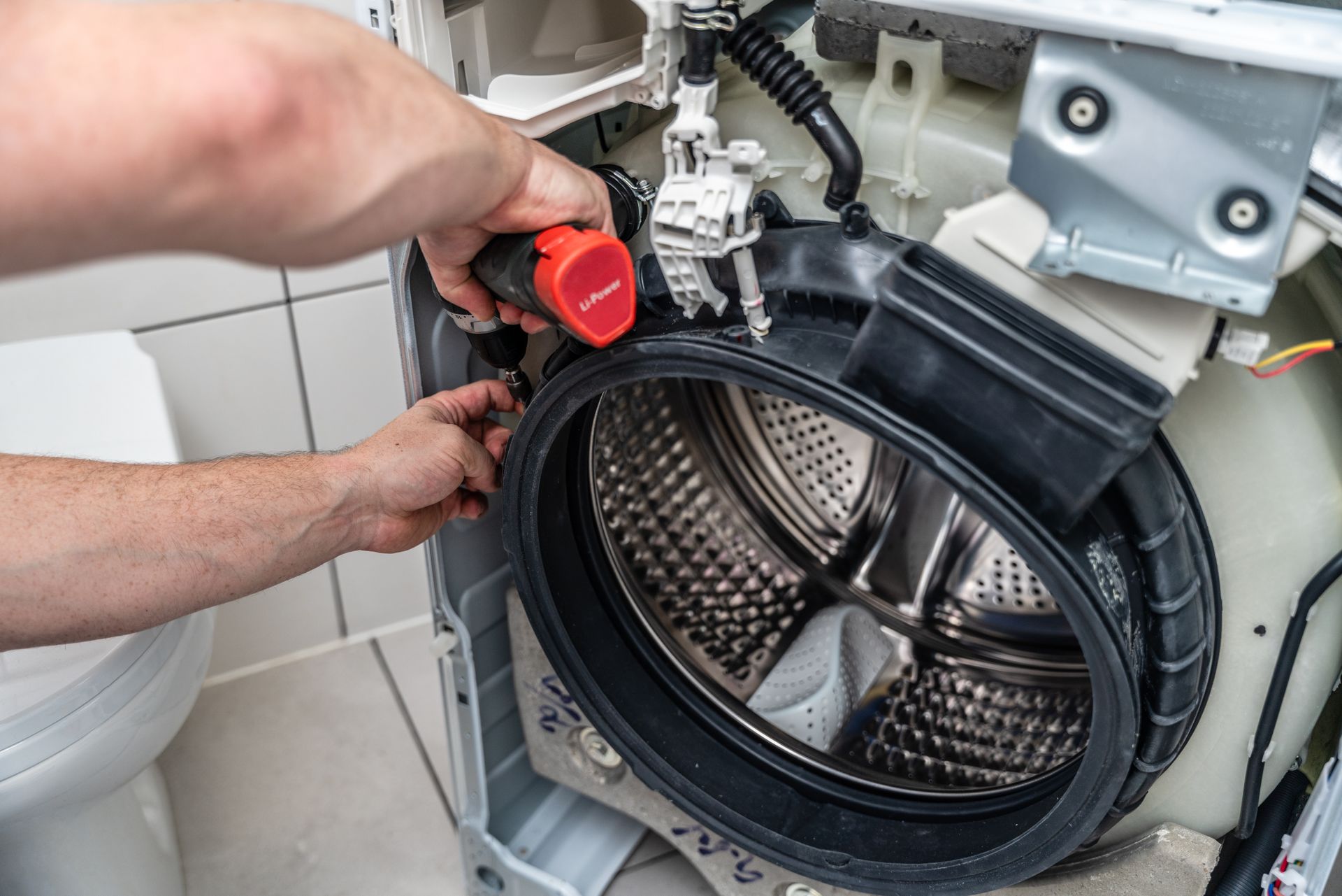 A man is fixing a washing machine with a screwdriver.