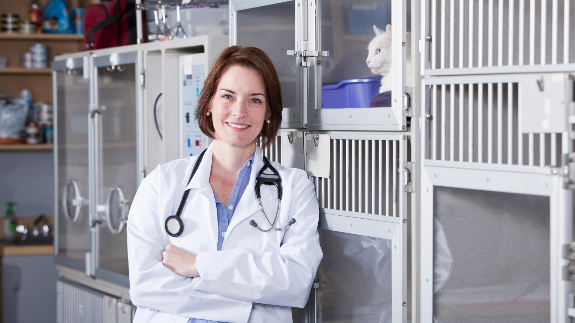 A female veterinarian is standing in front of a cage with a cat in it.