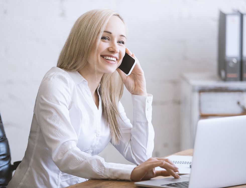 A woman is sitting at a desk talking on a cell phone.