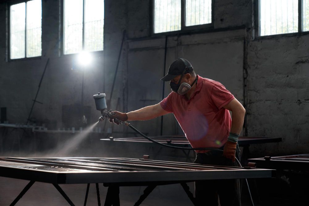A man is spray painting a piece of metal in a factory.