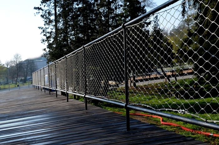 A metal fence surrounds a wooden walkway in a park.