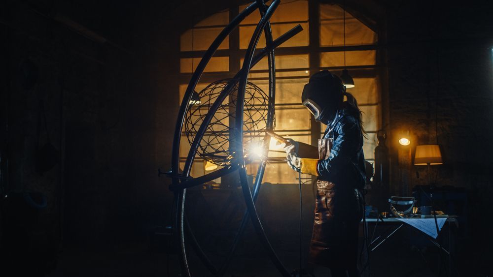 A man is welding a piece of metal in a dark room.