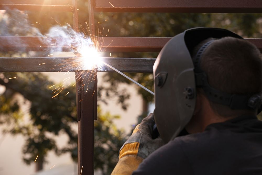 A man wearing a welding mask is welding a metal structure.