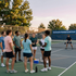 People gathered on an outdoor court for a social pickleball game at sunset