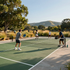 People playing pickleball on an outdoor court with mountains and trees in the background