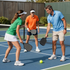 Three people play pickleball on a blue court, ready to hit a yellow ball.