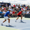 Two tennis players in blue and red rally on a court before a seated crowd