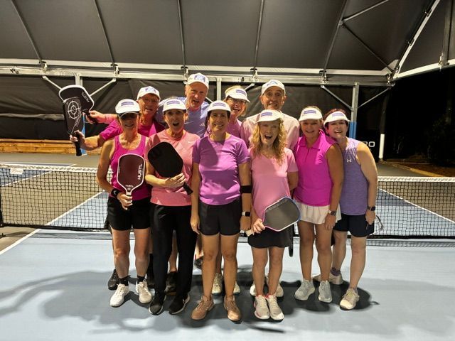 Tennis team in pink shirts posing with rackets under a court canopy at night