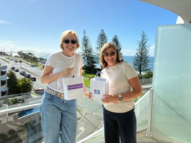 Two people holding boxes on a balcony with ocean and road views behind them