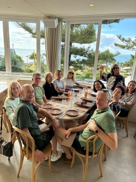 Group seated around a dining table in a bright beachfront room with ocean views and palm trees outside