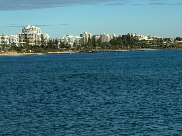 Blue ocean with a distant beachfront skyline of white high-rise buildings under a clear sky