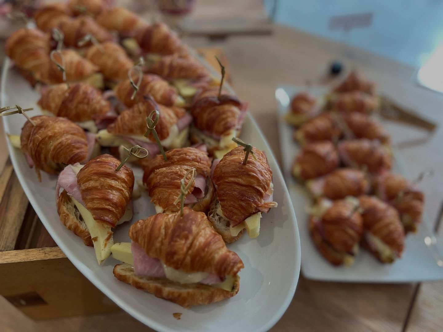 Platter of croissant sandwiches with ham and cheese, arranged on white serving dishes at a buffet.