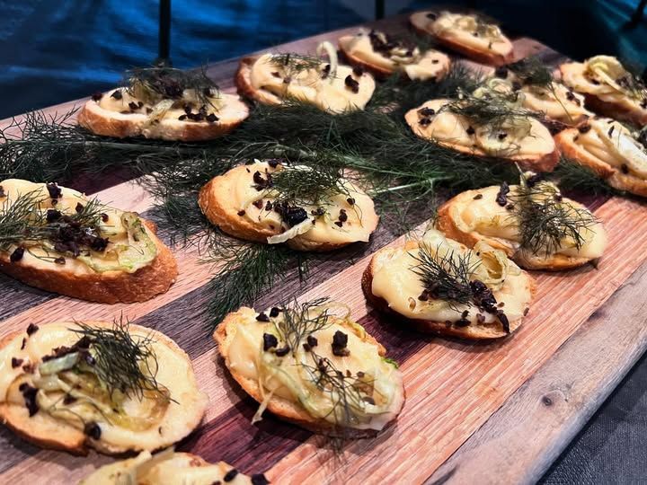 Baked herbed mini toasts on a wooden board, topped with cheese and sliced toppings