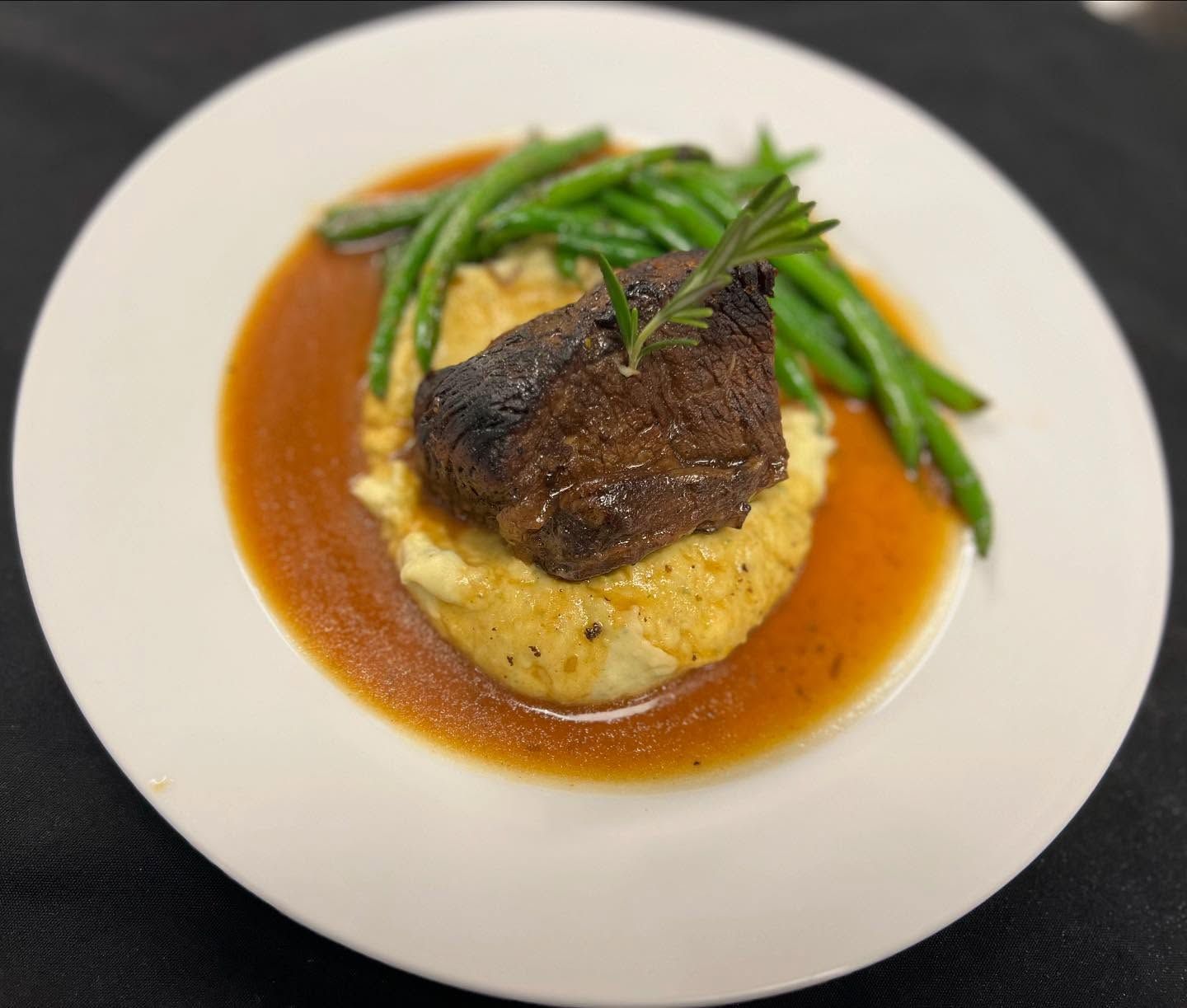 Plated beef steak over mashed potatoes with green beans and brown sauce on a white plate
