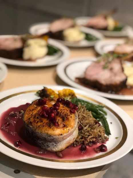 Plated gourmet meal with seared fish, red sauce, greens, and blurred dishes in the background