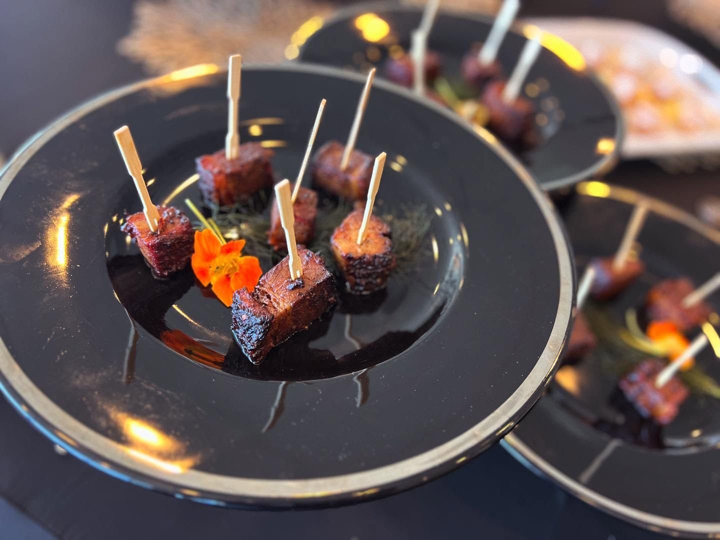 Plated appetizer bites with toothpicks on black dishes, topped with red garnish