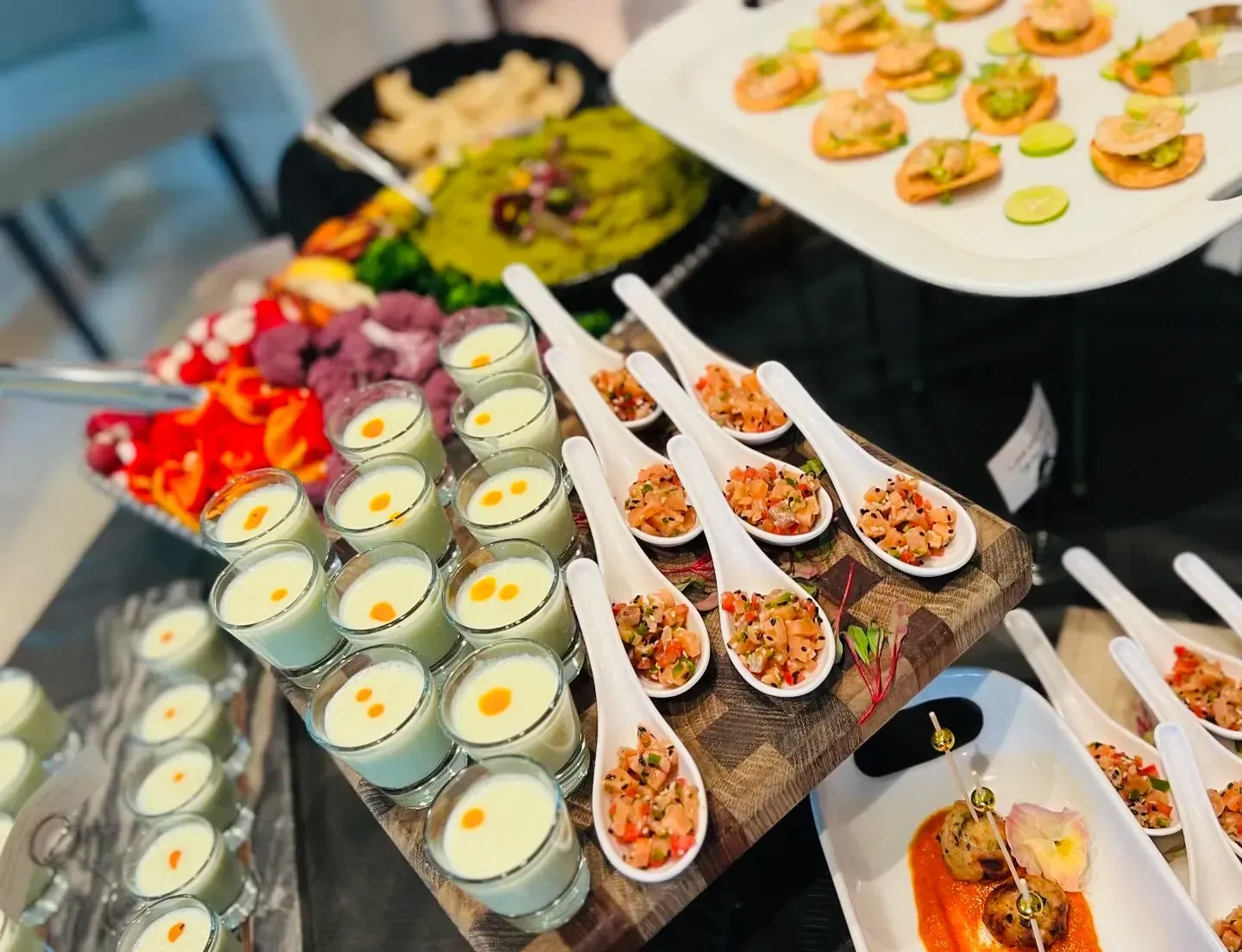 Assorted appetizers and desserts on a buffet table, including mini cups, spoons, and colorful garnishes.