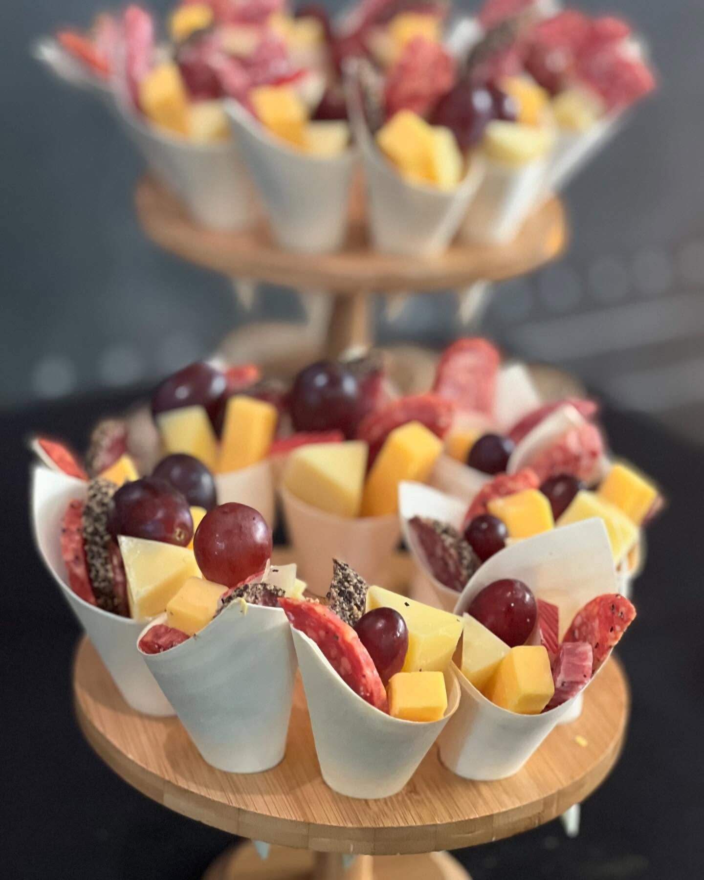 Two-tier dessert stand with cups of fruit, grapes, mango, and strawberries on a table