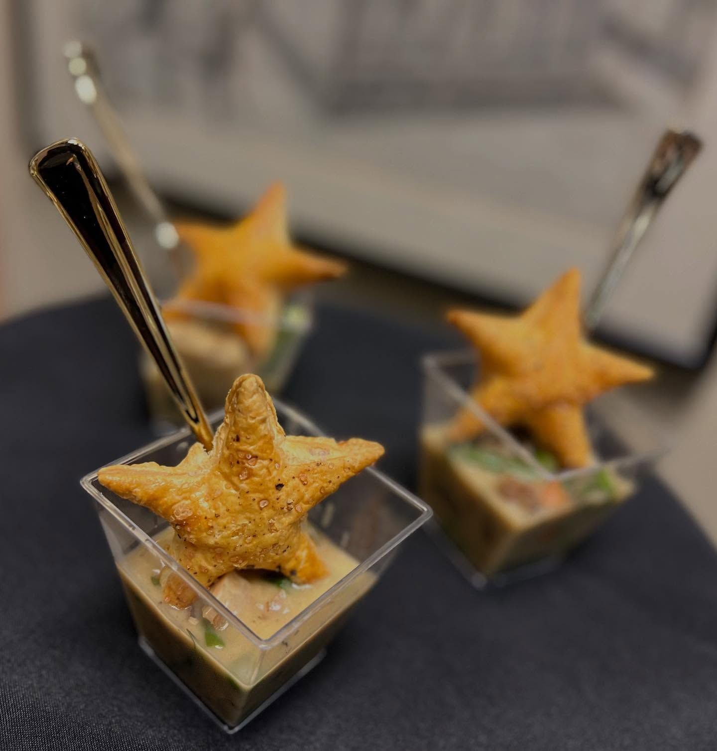 Three star-shaped pastries in clear cups with silver spoons on a dark tablecloth