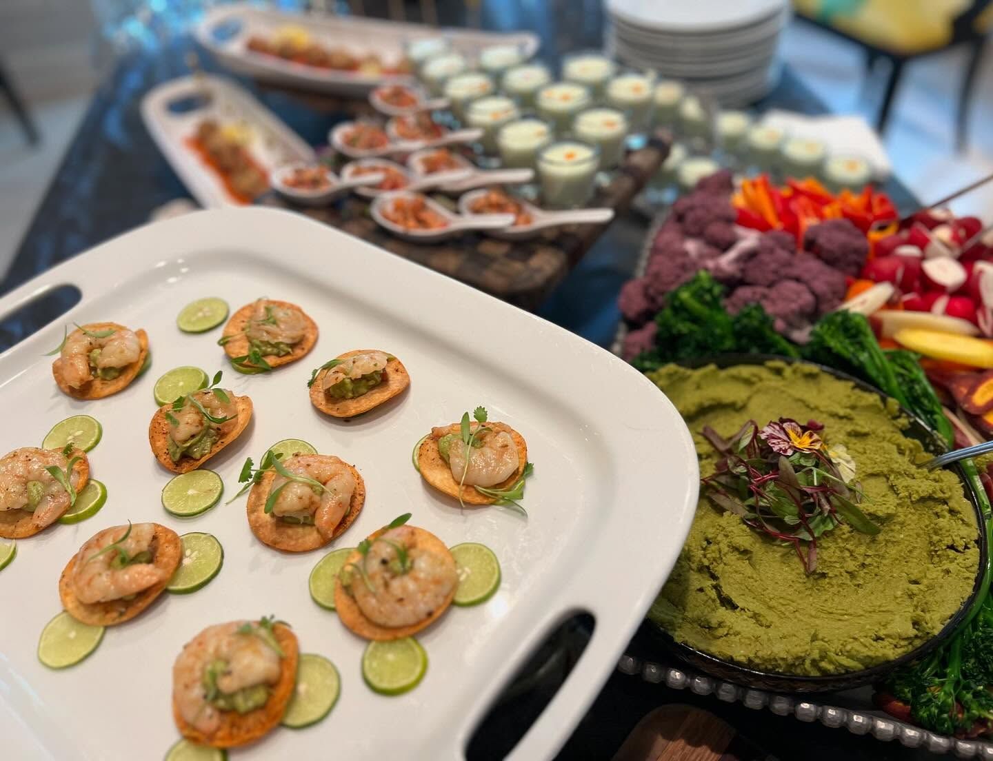 Platter of appetizers and dips on a buffet table, including shrimp crostini, hummus, and assorted vegetables.