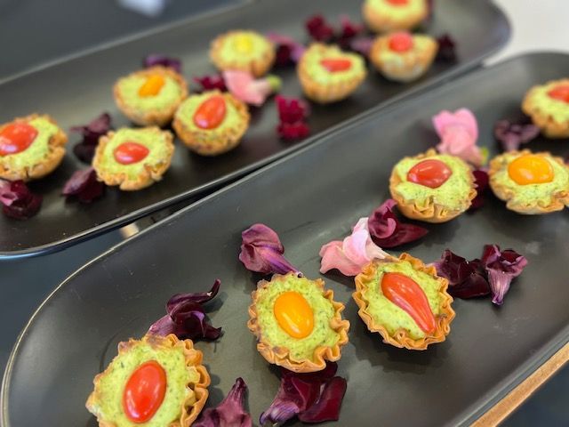 Mini tartlets topped with colorful fruit and flowers on black serving trays