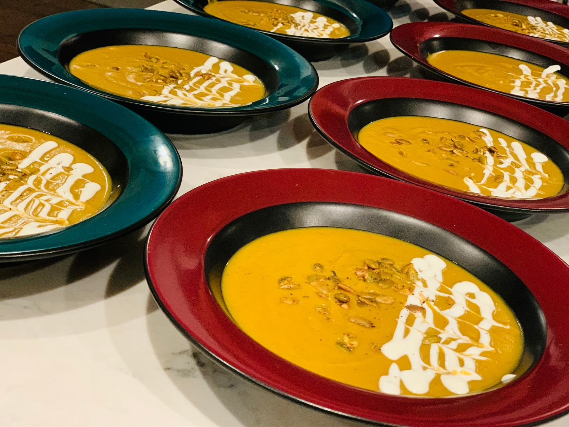 Several bowls of creamy soup with white drizzle on a table, in teal and red bowls.