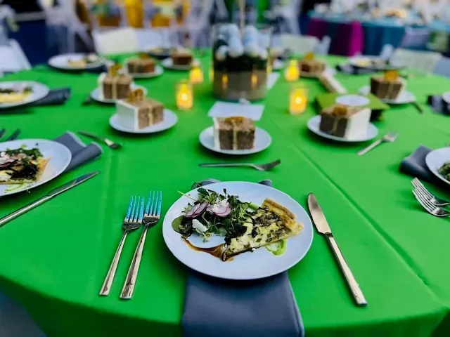 Banquet table with green tablecloth, plated salads, forks, knives, and candles in the center